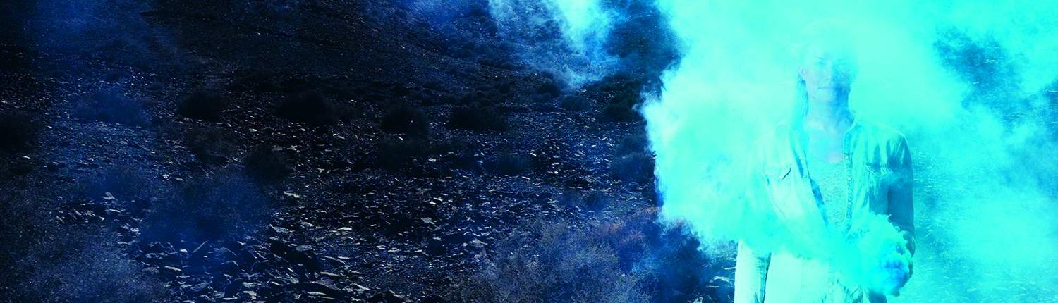 Woman standing in blue skies and blue smoke in the desert